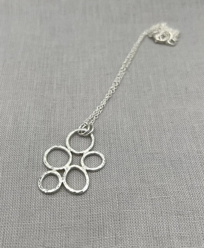 Textured silver pebble necklace with interlinked open circles on a fine chain, on grey fabric.