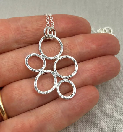 Hand holding a hammered silver circle pendant necklace on a light background