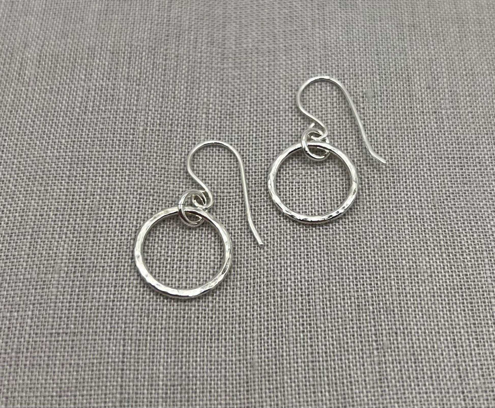 Handmade silver hoop earrings with hammered texture on grey fabric background