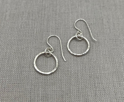 Handmade silver hoop earrings with hammered texture on grey fabric background