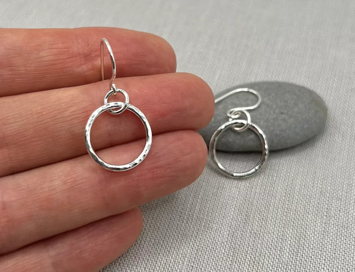 Handmade silver interlinked hoop earrings with hammered texture, displayed on fabric