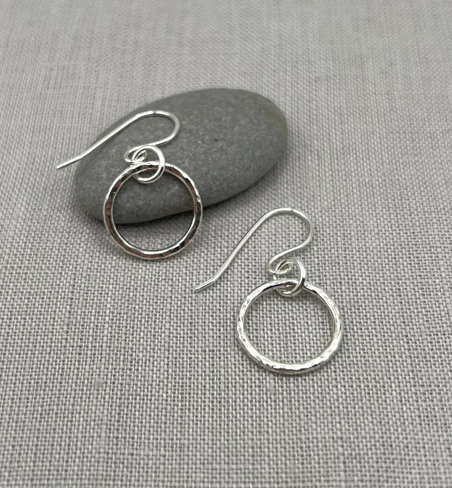 Handmade silver hoop earrings with textured finish on a grey fabric background