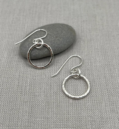 Handmade silver hoop earrings with textured finish on a grey fabric background