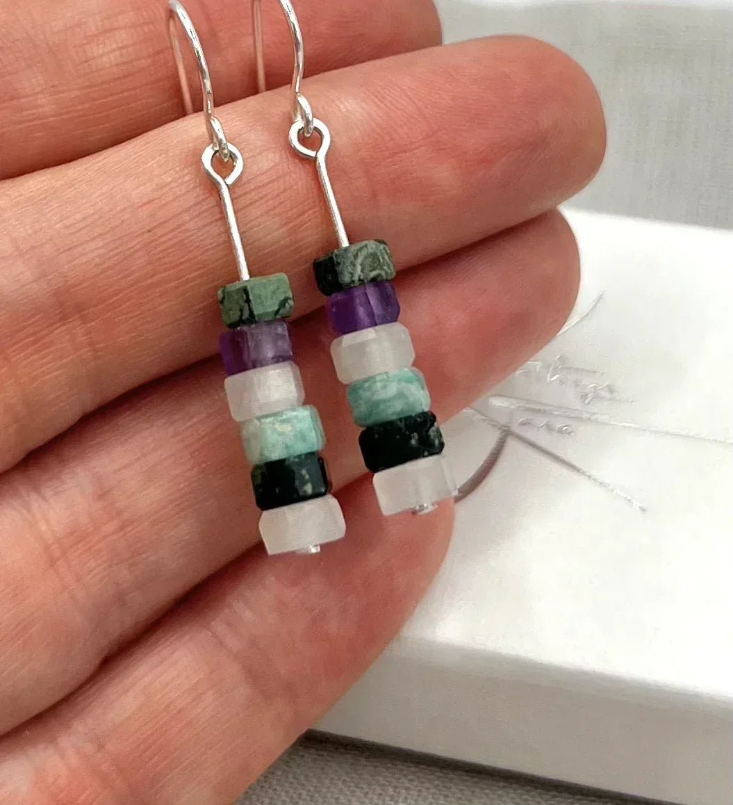 Hand holding dangle earrings with stacked purple, aqua, green, and white stone beads