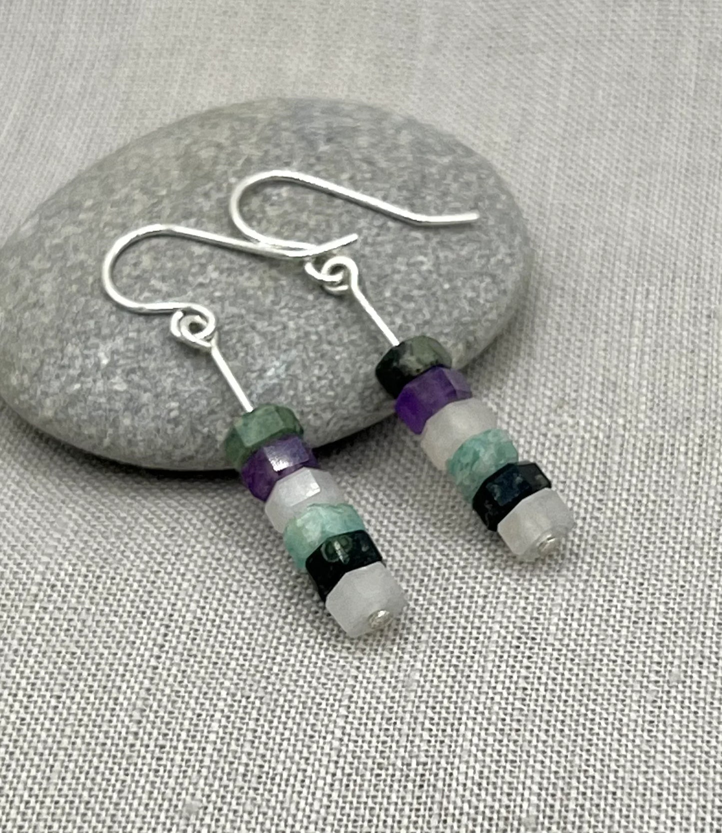 Silver hook earrings with stacked purple, aqua, and stone beads on a grey fabric background
