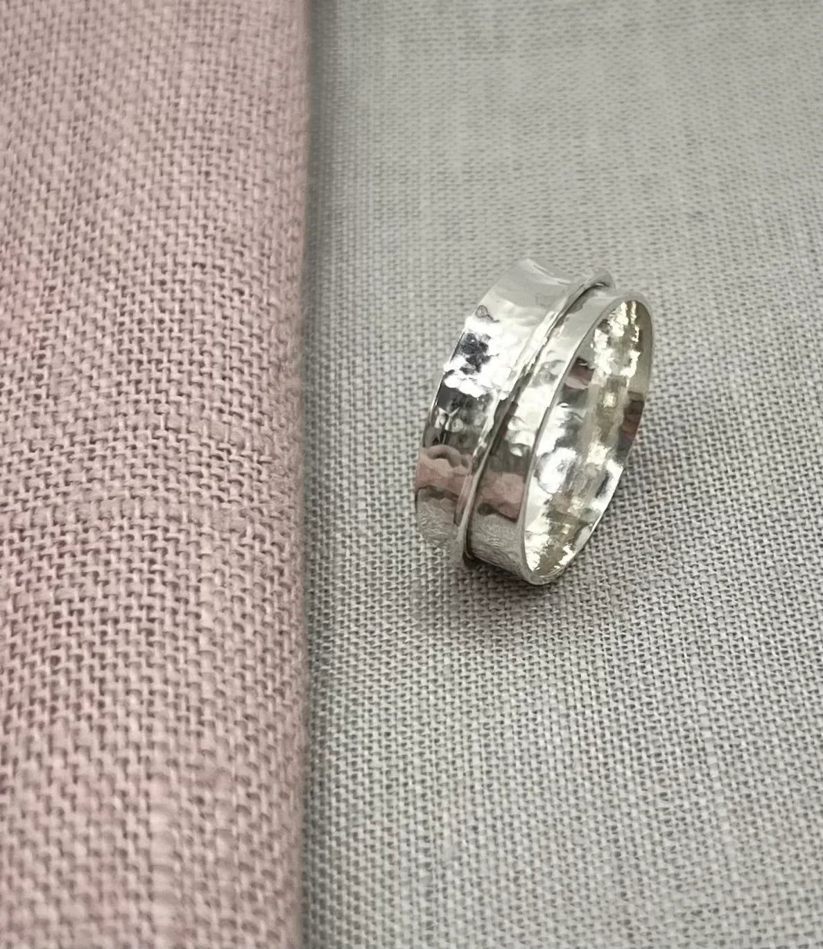 Handcrafted silver spinner ring with hammered texture on neutral fabric background