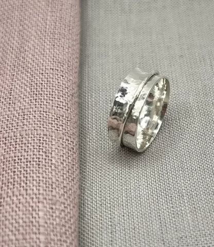 Handcrafted silver spinner ring with hammered texture on neutral fabric background