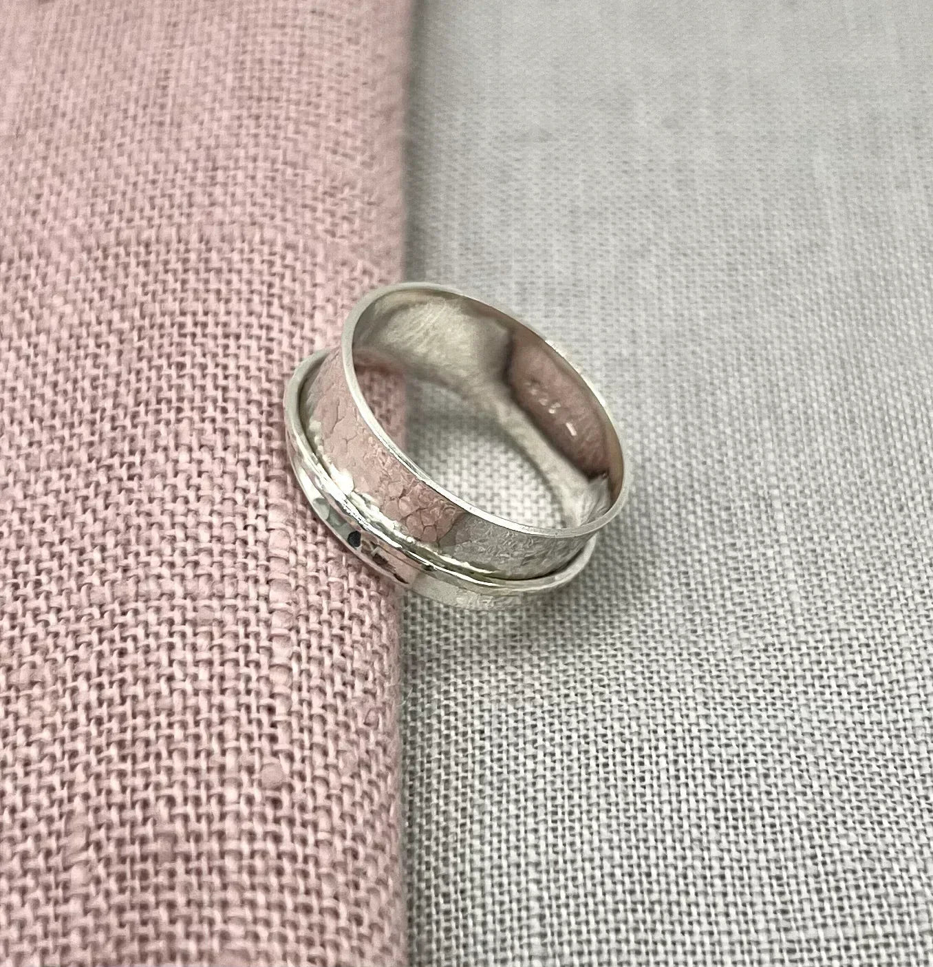 Handcrafted silver spinner ring with a textured band on pink and grey fabric background