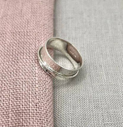 Handcrafted silver spinner ring with a textured band on pink and grey fabric background