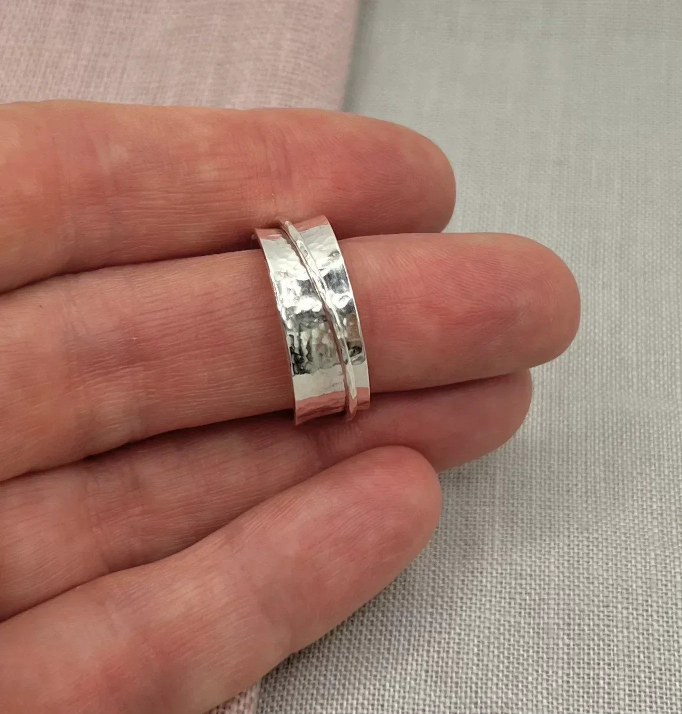 Hand holding a hammered silver spinner ring with textured band on neutral fabric background
