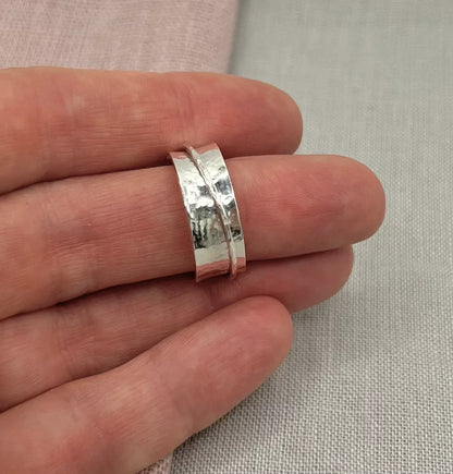 Hand holding a hammered silver spinner ring with textured band on neutral fabric background