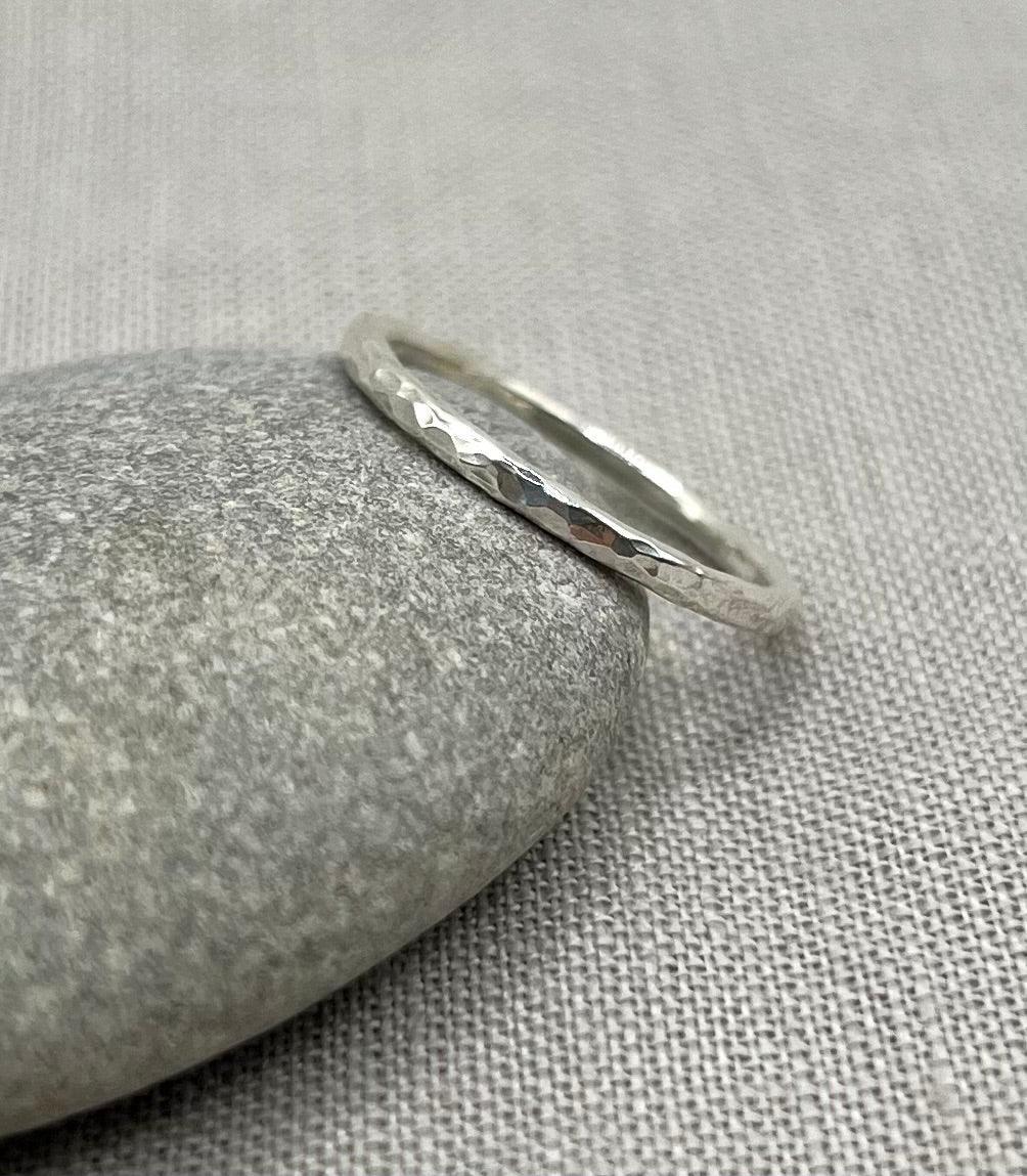 Delicate textured silver stacking ring displayed on a smooth stone over a fabric background
