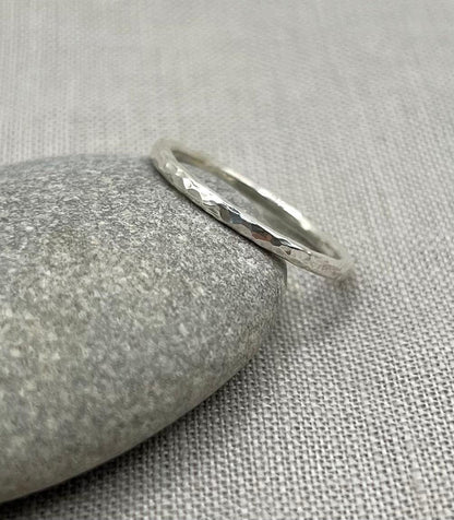 Delicate textured silver stacking ring displayed on a smooth stone over a fabric background
