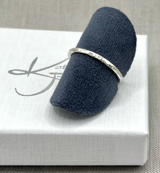 Silver ring on a navy blue cushion with a white box in the background