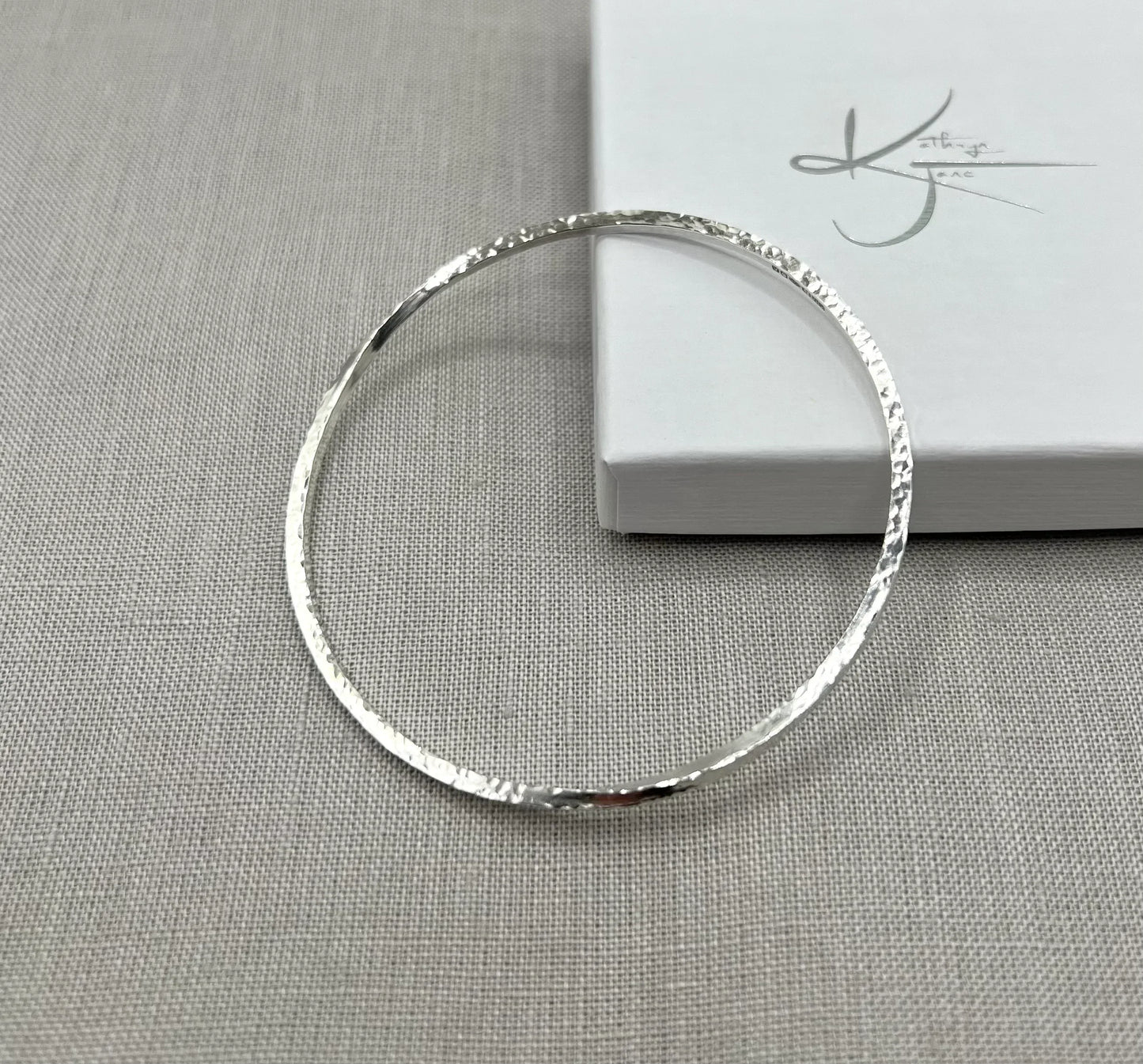 Textured silver twist bangle bracelet displayed on grey fabric beside a white gift box