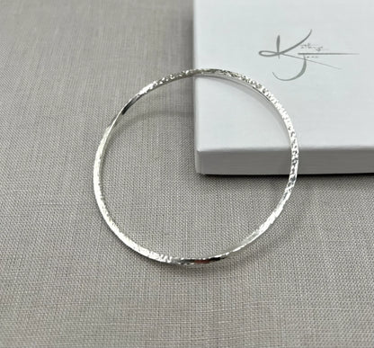 Textured silver twist bangle bracelet displayed on grey fabric beside a white gift box