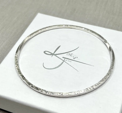 Hammered silver bangle bracelet with twisted design on a white jewellery box