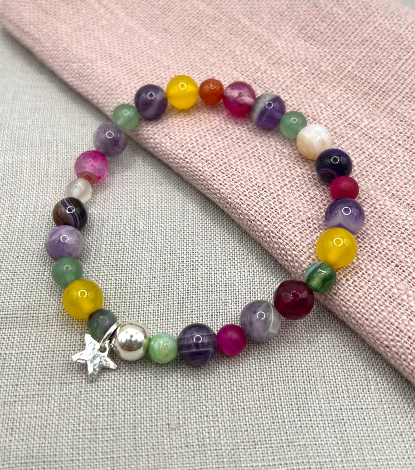 Multicolored beaded bracelet with a star charm on a light gray surface.
