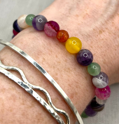 Multicolored beaded bracelet on a wrist with a silver bangle.