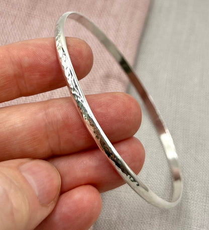 Silver bangle held in a hand against a neutral background