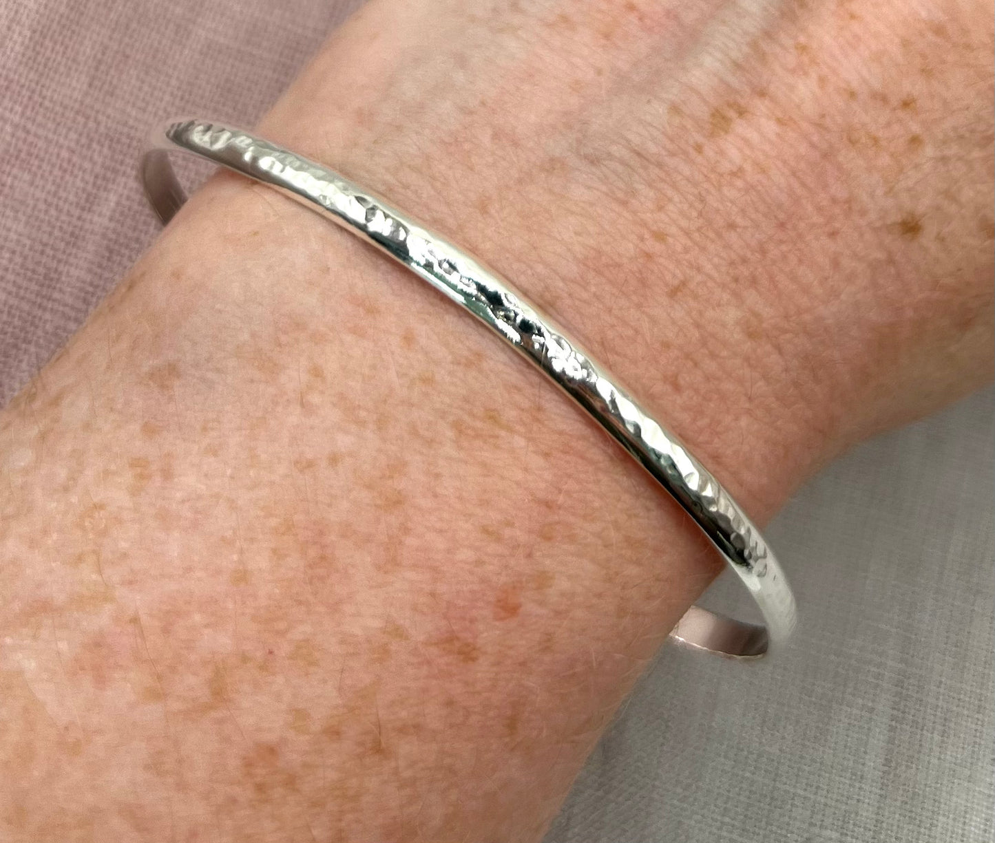 Silver bangle on a wrist with a neutral background