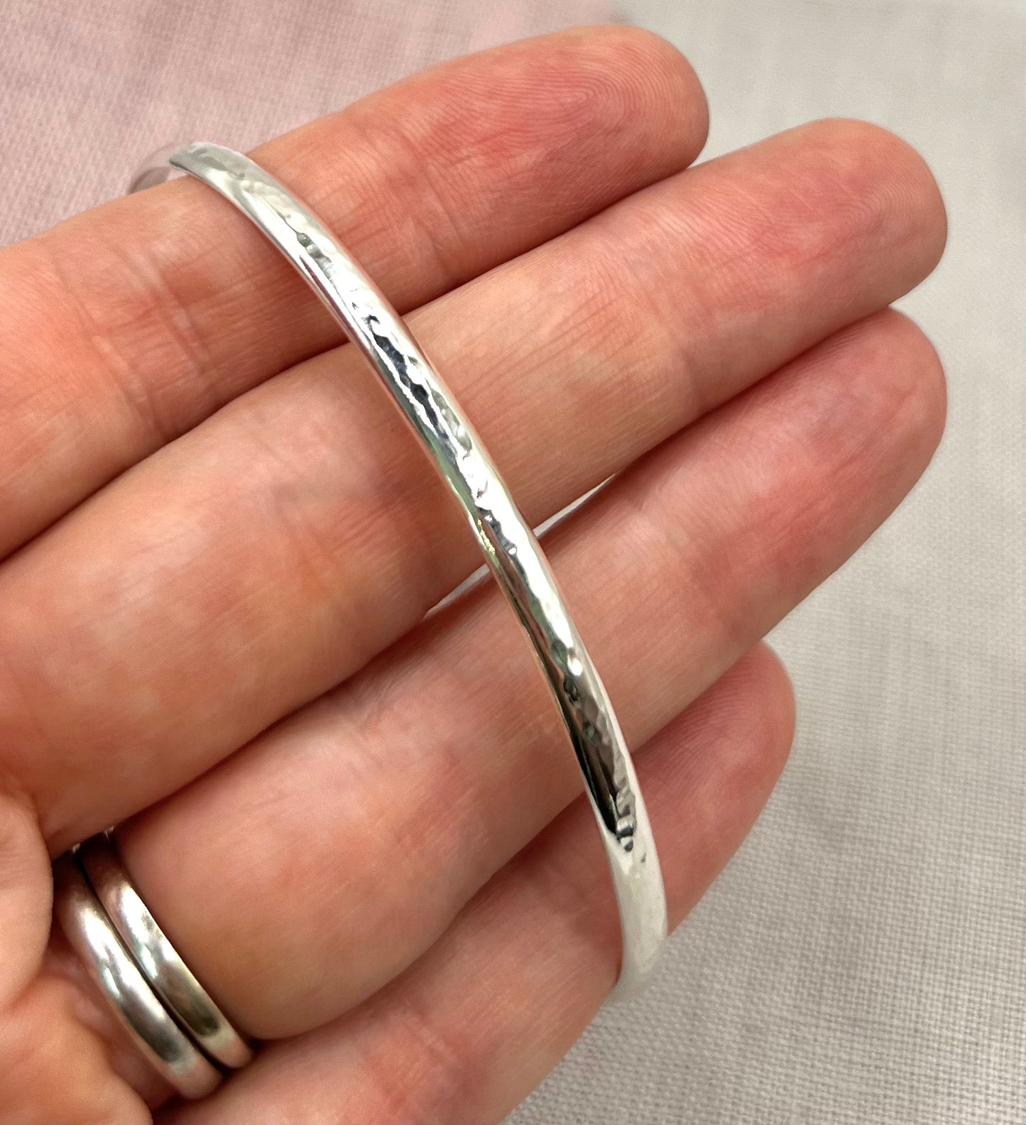 Silver bangle on a hand against a neutral background