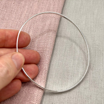 Silver bangle held by a hand on a textured fabric background
