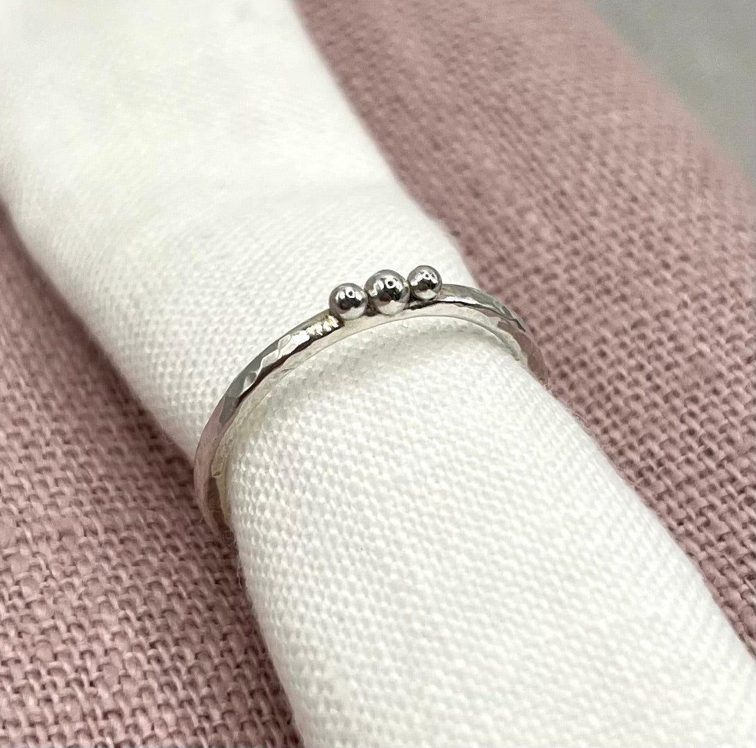 Silver ring with three small balls on a white linen against a textured pink background
