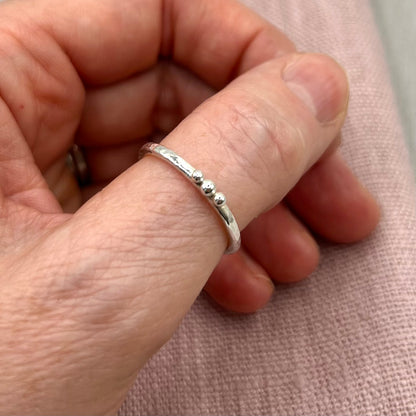 Silver ring on a finger against a pink fabric background